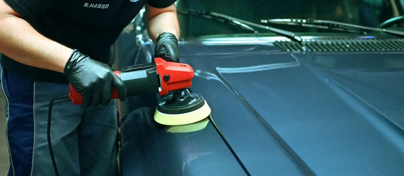 Detailer polijst de motorkap met een polijstmachine